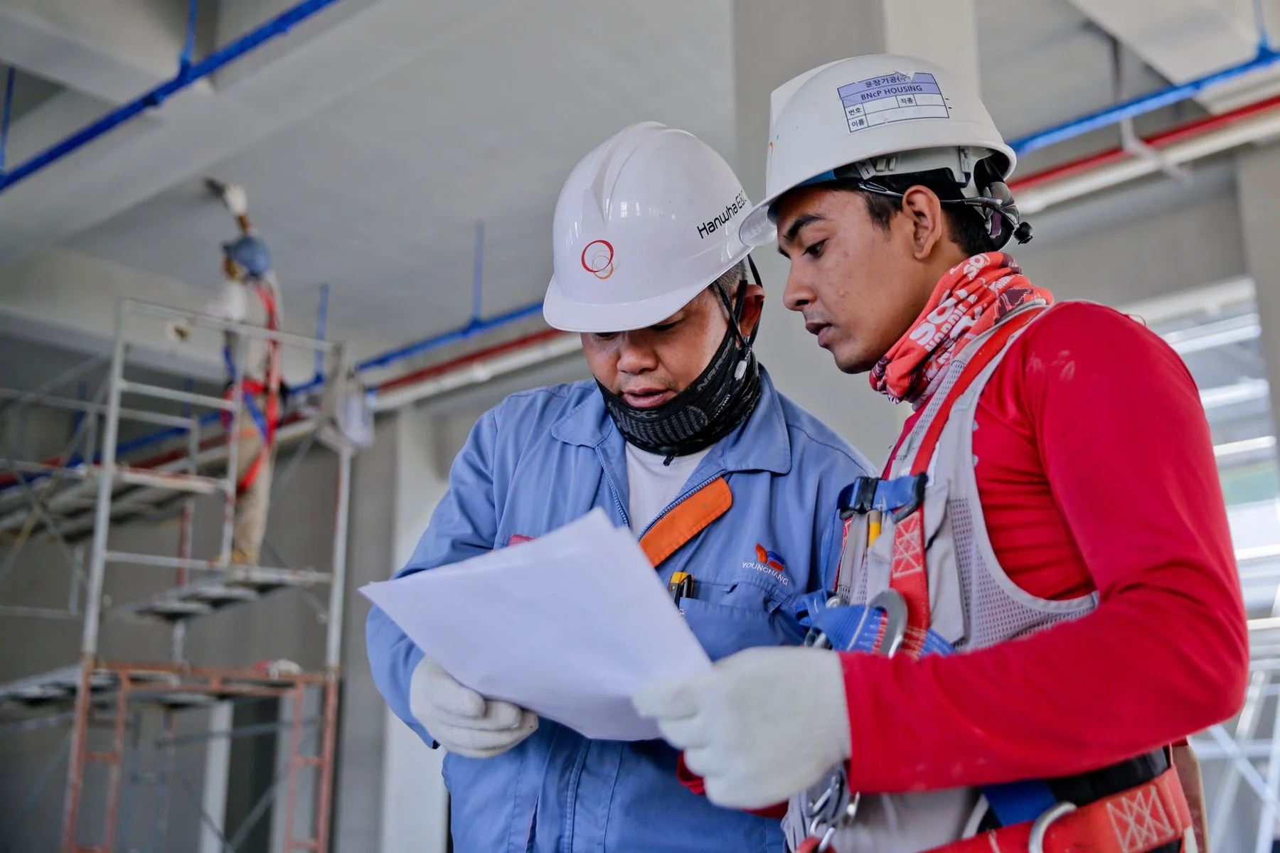 Two people in hard hats reviewing drawings indoors at a worksite