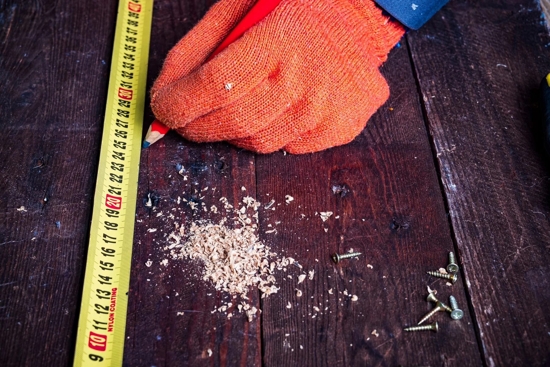 Gloved hand with measuring tape, pencil and fixings on timber