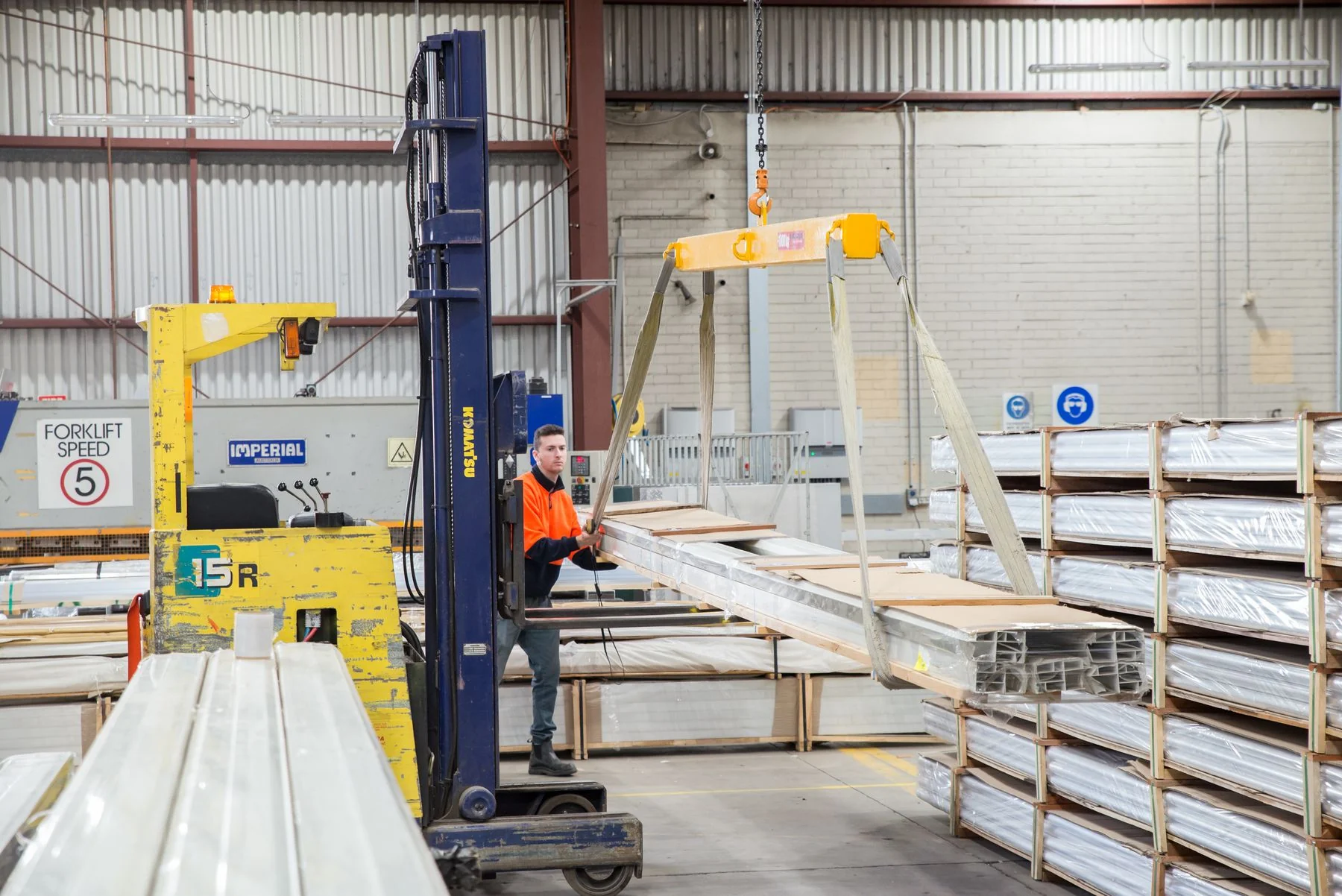 Worker and lifting equipment moving long metal material inside a factory