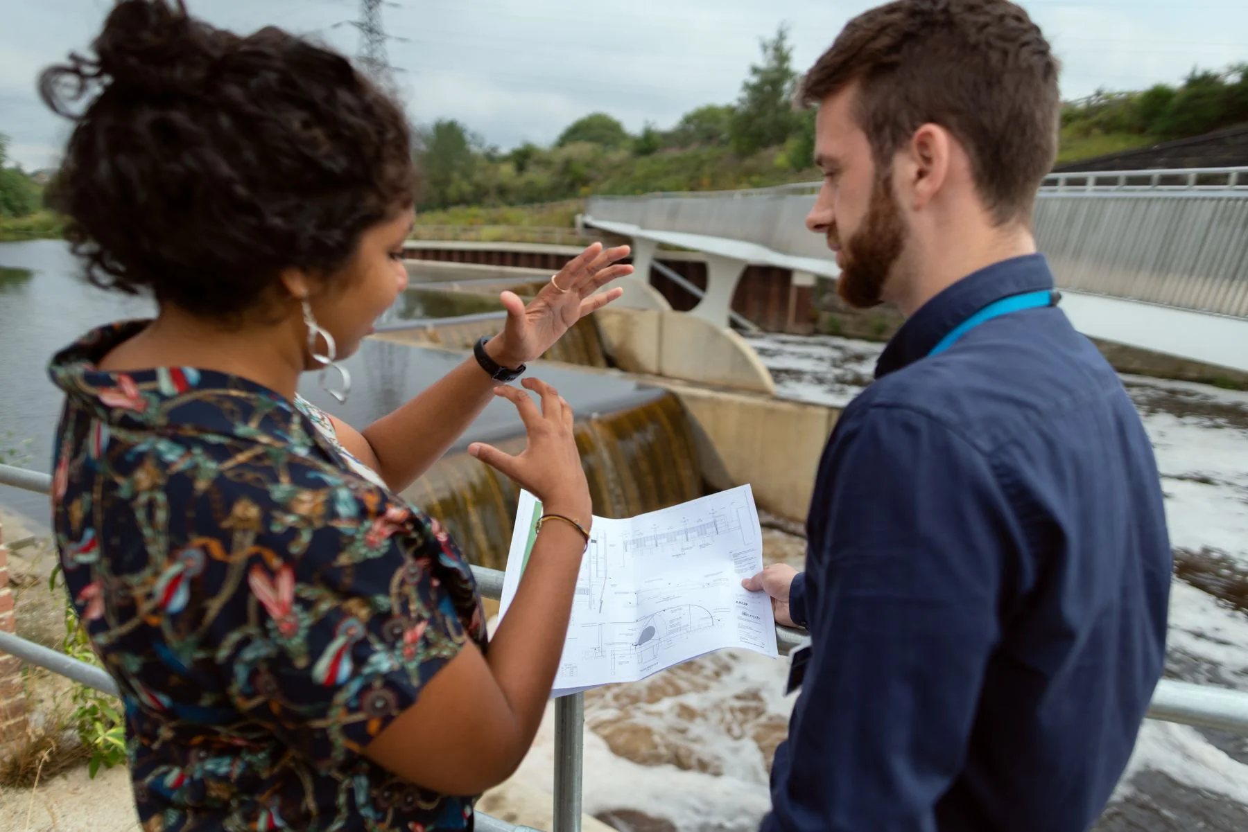 Two people discussing drawings beside water infrastructure