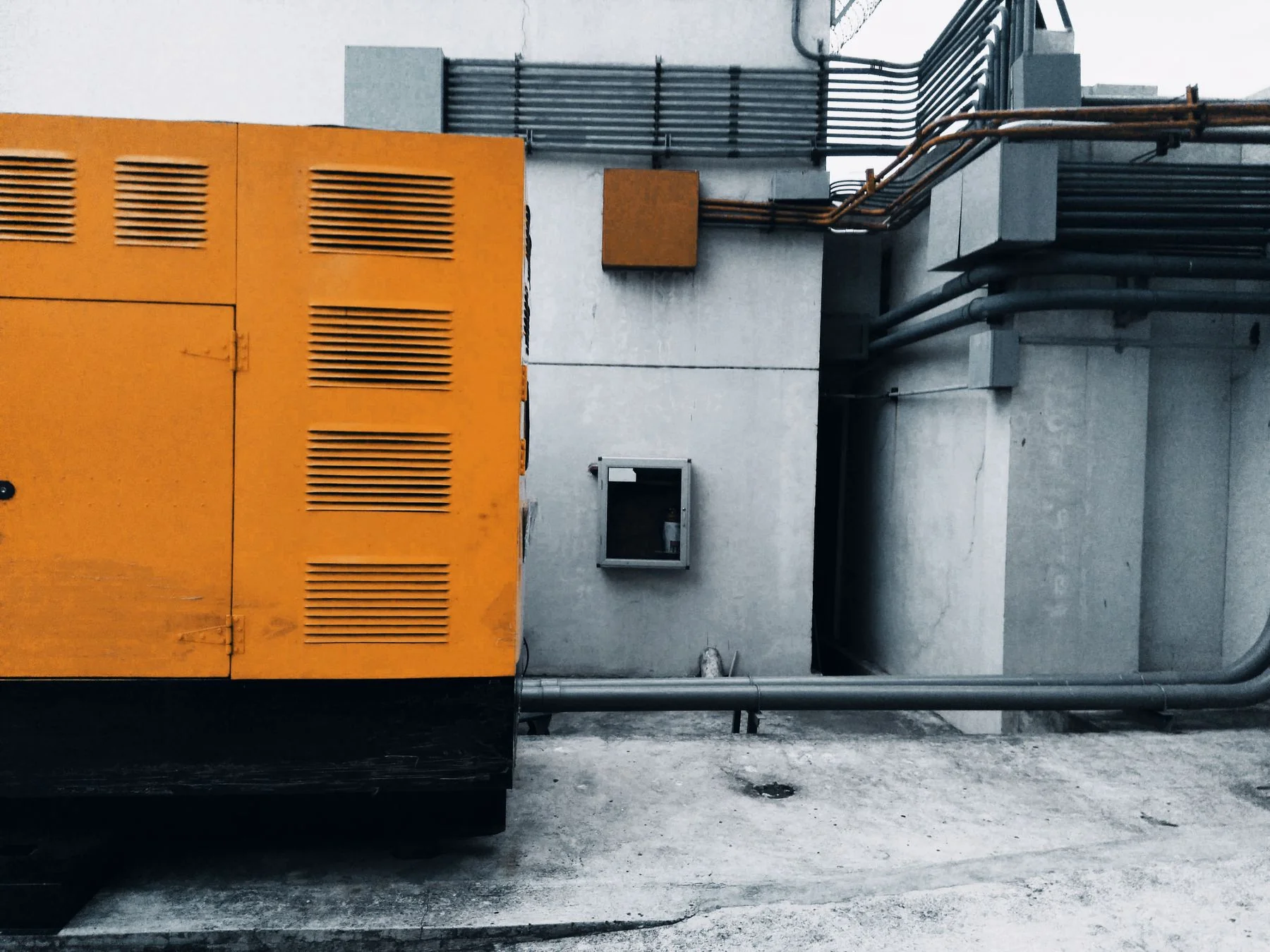 Yellow ventilated equipment enclosure beside fixed conduit and pipework