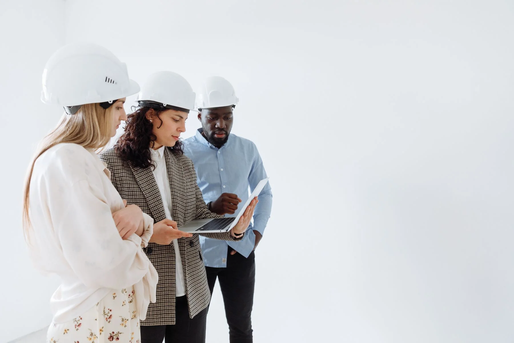 Three people in hard hats reviewing a laptop and papers indoors