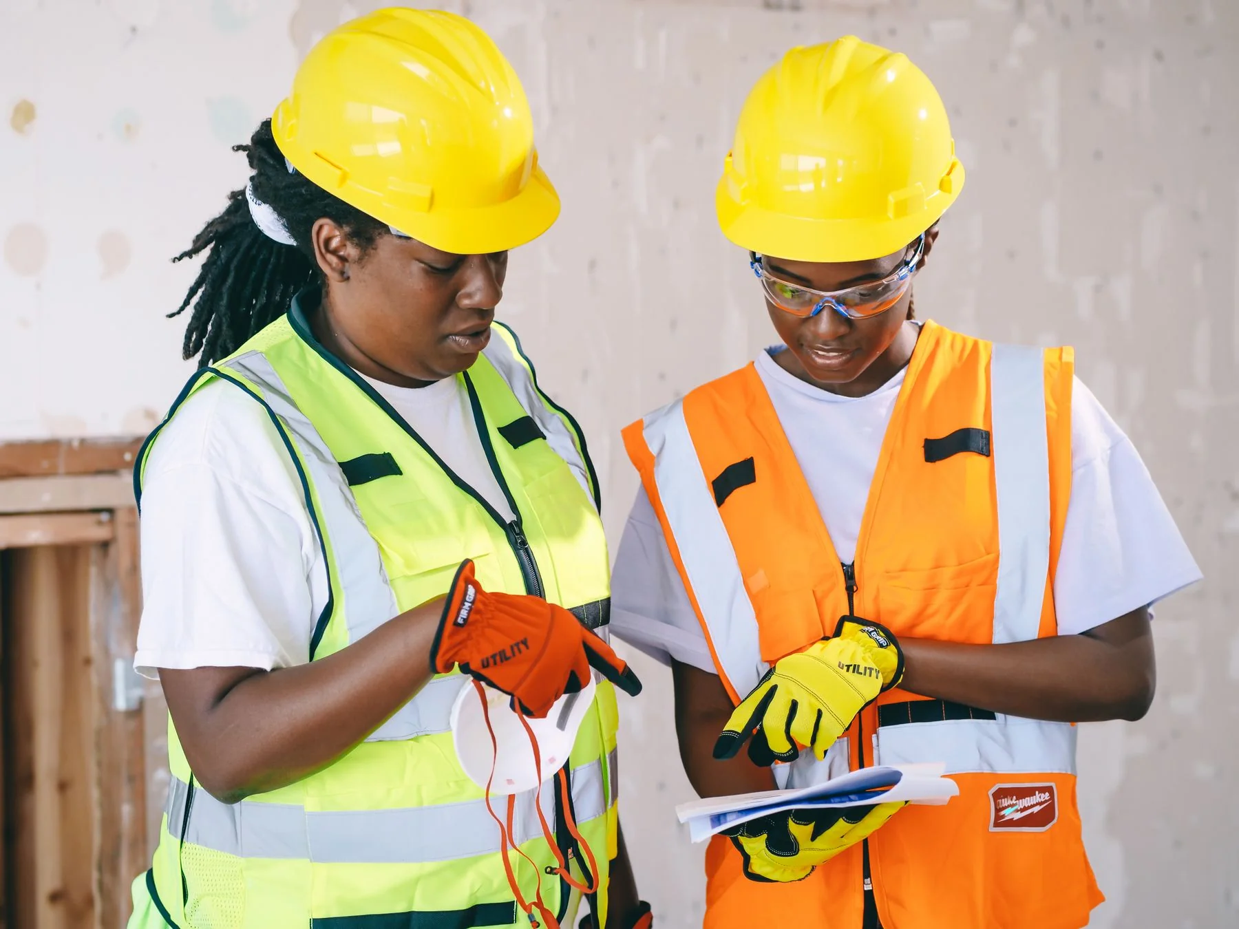 Two workers reviewing documents at an unfinished wall